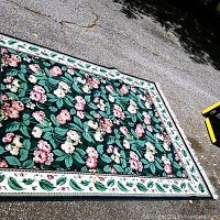 Full view of the floral area rug laid out on an asphalt driveway showing size, colors, and border design.