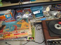 Photo of stacked classic board games including Battleship, Hangman, and Jutland naval combat games, with plastic containers and model crafting items in the background