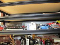 Shelf with a black limousine toy, blue Volkswagen Beetle toy car, and collectible toy tankers with original packaging.