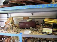 Full view of two shelves with assorted costume jewelry including boxes, bracelets, necklaces, rings, earrings, cuff links and watches spread out to show variety and quantity.