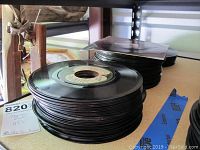 Stacked black 7-inch vinyl records in plastic sleeves and without sleeves, showing record labels and some wear.
