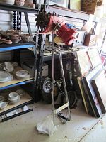 Full view of Mantis gas powered tiller standing upright near shelving with various dishes and picture frames.