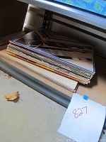 Stack of vinyl records with visible album covers, showing wear and storage on shelf.