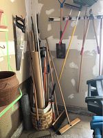 View of yard tools leaning against wall, including saw, handles, and rakes.