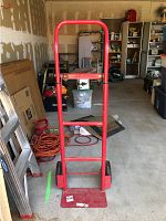 Front view of the red metal hand truck standing upright in a garage.