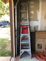 Two ladders positioned against a wall showing their relative sizes, with a step ladder in front and extension ladder behind.