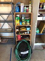 Wooden shelf with assorted gardening supplies and coiled green garden hose on floor