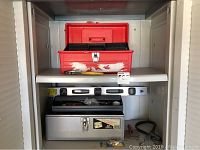 Photo shows red plastic toolbox with worn paint, metal toolbox below it, level on bottom shelf, some small tools and pliers in front.