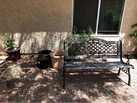Shows outdoor scene with outdoor bench to the right and four pots of various sizes and colors to the left, near a stone and stucco wall, with potted plants inside some pots.