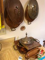 Photo showing wall-mounted 13-inch and 12-inch copper pots with lids, brass handles, with wooden and copper trays and decorative items on kitchen counter.