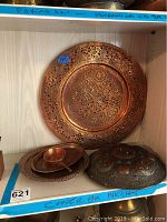 Wide view of shelf displaying the large decorative copper plate, smaller copper dishes, and wooden carved item with turquoise inlays.