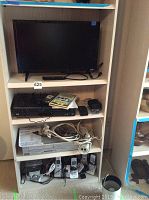 Full view of wooden shelving with all electronics including TV, DVD VHS player, telephones, power strip, and cables.