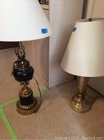 Two vintage brass lamps placed side by side on a carpeted floor, showing overall appearance and fabric shades.