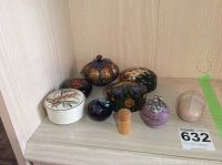 Photo of nine assorted small trinket boxes displayed on a shelf ranging in design from floral to colorful Indian-style ornamentation, including wood and ceramic materials.