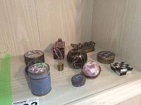 Photo of eleven assorted small trinket boxes placed on a wooden shelf corner, showing metal and stone materials with various colors and shapes.