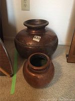 Photo showing both copper pots together, one larger bulbous pot with wide mouth and a smaller round pot in front.