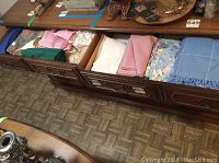 Drawer filled with assorted folded table linens in various colors including pink, green, white, and floral patterns