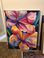Full front view of the colorful floral acrylic painting on canvas leaning against a wall, showing vibrant pink, purple, orange, yellow, and blue hues.
