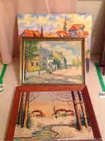 All three folk art paintings shown together; one large canvas painting in back, two framed paintings in front on a cloth surface.