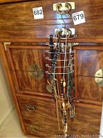 Assortment of costume jewelry necklaces hanging on metal rack attached to wooden furniture with brass handles