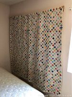 Full view of the quilt hanging showing overall patchwork pattern of small colored diamond fabric pieces framed with white fabric strips.