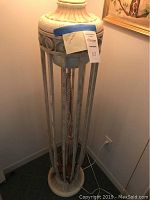 Full view of the tall floor lamp, showing the round base, vertical metal supports, decorative top, and rope pull chain hanging inside.