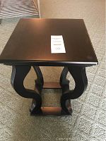 Front top view of the black accent table showing square tabletop with slight reflective finish and curved leg design.
