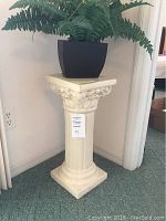 Full view of cream-colored pillar accent stand with a plant on top, showing overall design and shape.