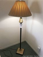 Full view of floor lamp with brown pleated shade and black stand on base with stone tile mosaic