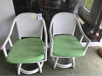 Pair of white wicker swivel chairs with green cushions, some cushion stains visible.
