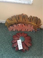 Three metal wall art pieces on carpet - two leaf designs and one flower design