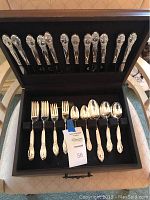 Open wooden box displaying polished forks, knives, and spoons by Oneida Silversmiths with ornate handles.