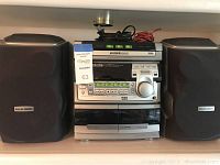 Full front view of the Philips Magnavox FW570C mini HiFi system showing left and right speakers, stereo unit in middle with 3-CD changer, cassette decks, radio controls and display.