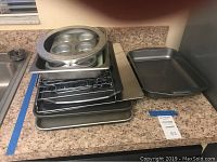 Stacked baking sheets, cupcake pans, and wire racks placed on kitchen counter surface.