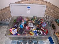 Clear plastic bin filled with a large assortment of individually packaged McDonald's Happy Meal toys featuring various characters and styles.
