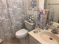 Full bathroom view showing toilet, shower curtain with seashell and starfish motif, and light blue metal toilet paper stand next to the sink.