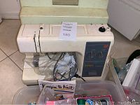 Top view of the Kenmore sewing machine showing model 22 control panel, power cord, and some included sewing supplies in front.