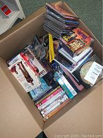 Top-down photo showing large cardboard box filled with mixed music CDs, movie DVDs, and books.