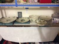 Wide shot showing all Lenox Holiday serving pieces and Mikasa poinsettia candy dish displayed on shelving.