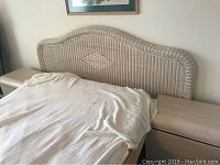 Wicker king size headboard with two matching nightstands on either side, bed partially shown covered with blanket.