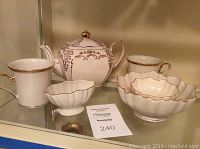 Full lot view showing teapot, two mugs, and three serving dishes on glass shelf.