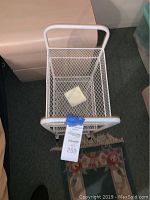 Top view of white wire mesh basket shelf and handle with a note inside the basket and auction tag on the handle.