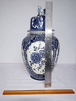 Front view of blue and white Delft style covered vase with ruler for scale showing about 15 inches tall.