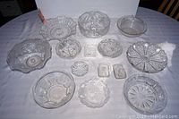 Front and top view of fourteen vintage glass and crystal bowls and dishes exhibiting varied intricate pressed and cut glass designs.