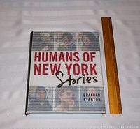 Front cover of the hardcover book 'Humans of New York Stories' by Brandon Stanton, alongside a ruler for scale.