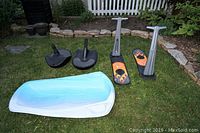 Full view of five sleds including one large white and blue sled, two black bum sleds, and two black and orange snowboard style sleds with handles folded up