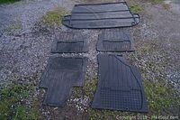 Five black rubber floor mats arranged on gravel outdoors, showing front driver, front passenger, two rear passenger mats and a cargo mat