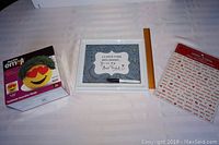 Photo showing all three items: message sign with marker, boxed Heart Eyed Chia Pet Emoji, and magnetic poetry set with words on board.
