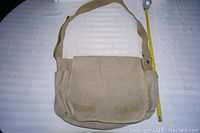 Full view of Rothko canvas messenger bag showing main flap, two side pockets, and adjustable shoulder strap with measuring tape to show length.