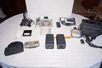 Top-down photo of all items showing Logitech Attack 3 controller, video cameras, multiple speakers, remote, power adapter, and carrying cases arranged neatly on a white table.